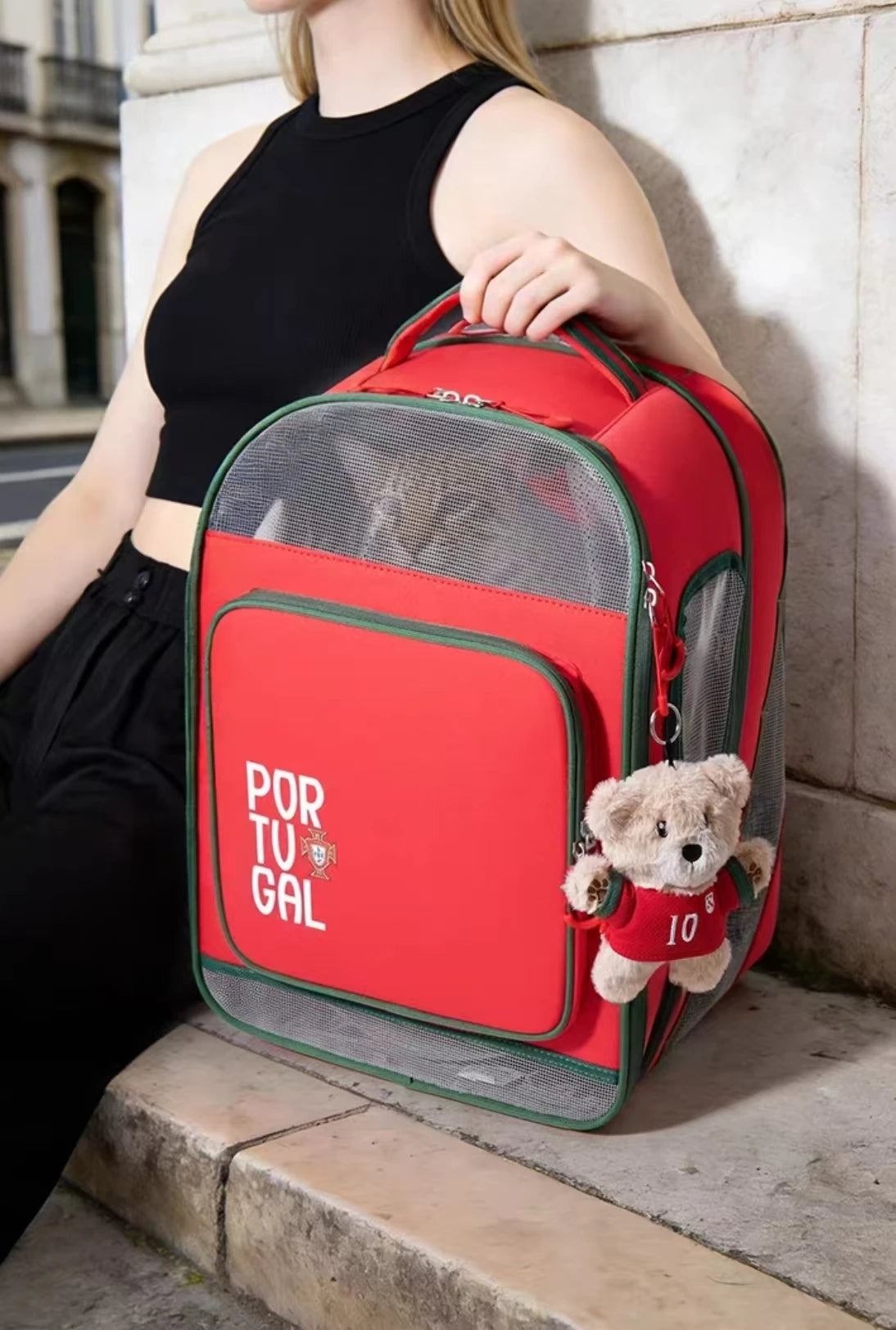 Petstar Portugal backpack held by its top handle beside a decorative bear
