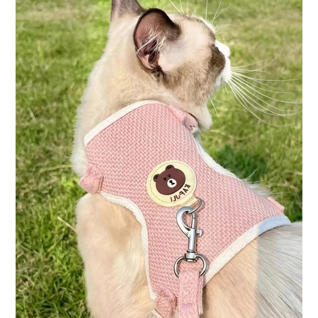 Cat wearing pink vest harness on grass